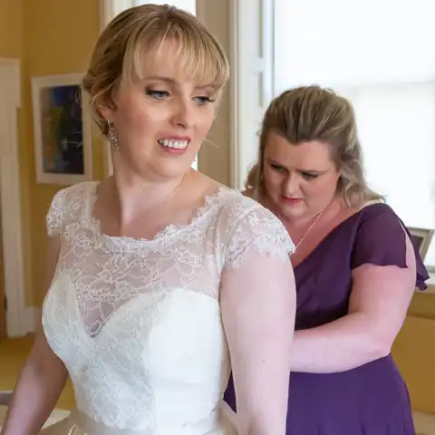 Wedding photo of the bridesmaids doing up the buttons on the brides dress at Childwickbury, St Albans, Hertfordshire.  – photography by Glen Smith