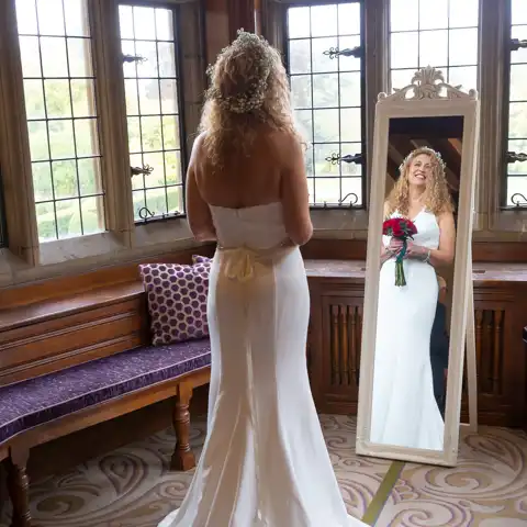 Wedding photo of the bride getting ready, looking in a mirror at Fanhams Hall, Ware, Hertfordshire.  – photography by Glen Smith