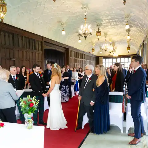 Wedding photo of the bride and groom and guests in the ceremony in the splendid Long Gallery at Fanhams Hall, Ware, Hertfordshire.  – photography by Glen Smith