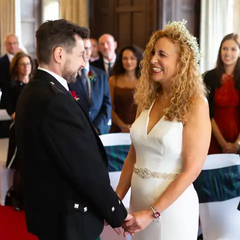 Wedding photo of close up of the bride and groom exchanging vows and smiling at each other and holding hands at Fanhams Hall, Ware, Hertfordshire.  – photography by Glen Smith