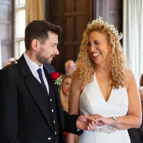 Wedding photo of the bride and groom holding hands in the Long Gallery in the ceremony and smiling at each other at Fanhams Hall, Ware, Hertfordshire.  – photography by Glen Smith