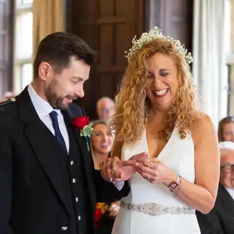 Wedding photo of the bride placing the ring on the grooms finger in the ceremony in the Long Gallery at Fanhams Hall, Ware, Hertfordshire.  – photography by Glen Smith