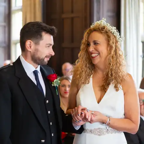 Wedding photo of the bride and groom holding hands in the ceremony in the Long Gallery at Fanhams Hall, Ware, Hertfordshire.  – photography by Glen Smith