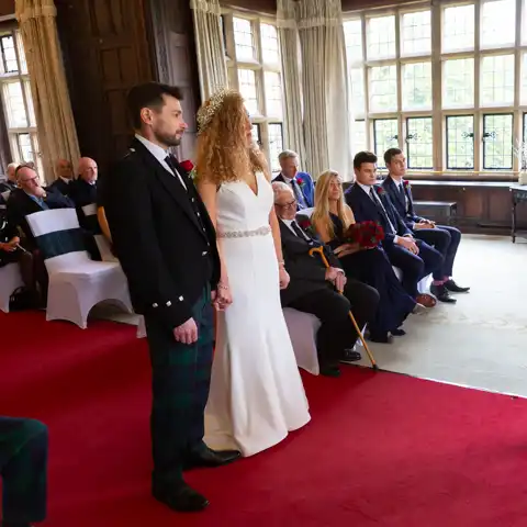 Wedding photo of the bride and groom and the registrar in the ceremony in the Long Gallery at Fanhams Hall, Ware, Hertfordshire.  – photography by Glen Smith