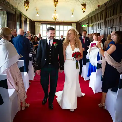 Wedding photo of the bride and groom walking down the aisle in the Long Gallery at Fanhams Hall, Ware, Hertfordshire.  – photography by Glen Smith
