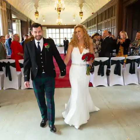 Wedding photo of the bride and groom walking down the aisle in the Long Gallery at Fanhams Hall, Ware, Hertfordshire.  – photography by Glen Smith