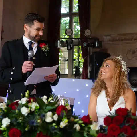 Wedding photo of the bride laughing and looking at the groom while he makes his wedding speech at Fanhams Hall, Ware, Hertfordshire.  – photography by Glen Smith