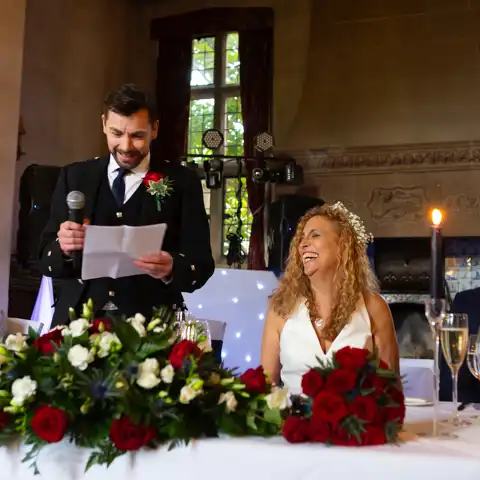 Wedding photo of the bride laughing and looking at the groom while he makes his wedding speech at Fanhams Hall, Ware, Hertfordshire.  – photography by Glen Smith
