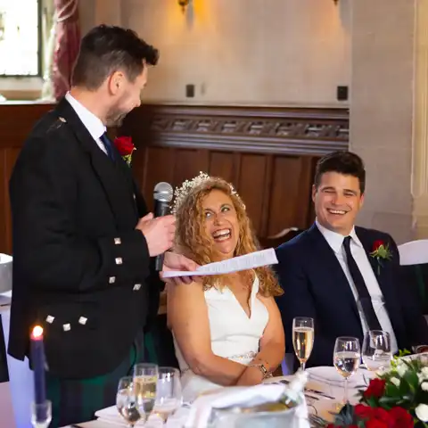 Wedding photo of the bride laughing and looking at the groom while he makes his wedding speech at Fanhams Hall, Ware, Hertfordshire.  – photography by Glen Smith