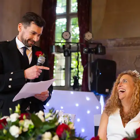 Wedding photo of the bride laughing and looking at the groom while he makes his wedding speech at Fanhams Hall, Ware, Hertfordshire.  – photography by Glen Smith